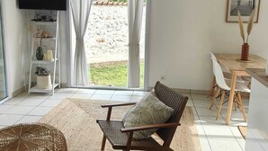 A modern living room with a large window, a flat-screen TV, a dining area with a wooden table and chairs, and a woven rug. - Sunny holiday in the quiet countryside with pool. (Lalbenque)