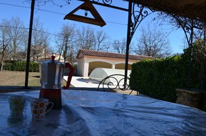 A table with a coffee maker and two cups, a metal pergola, and a building with a tiled roof in the background. - Sunny holiday in the quiet countryside with pool. (Lalbenque)