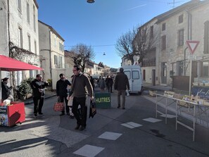 A street scene with pedestrians, a white van, and a 'HUITRES' sign indicating a hotel. - Sunny holiday in the quiet countryside with pool. (Lalbenque)