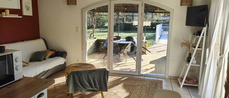 A living room with a sofa, a dining table, a TV, and a sliding glass door leading to an outdoor patio.