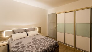 Un dormitorio con cama, mesitas de noche, un armario con paneles de vidrio esmerilado y una lámpara en el techo.