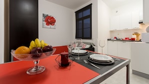 Una cocina moderna con gabinetes blancos, una mesa de comedor lista con platos, vasos y un frutero.