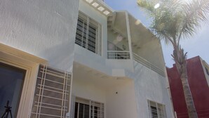 Un edificio de varios pisos con un balcón, una palmera y una puerta.