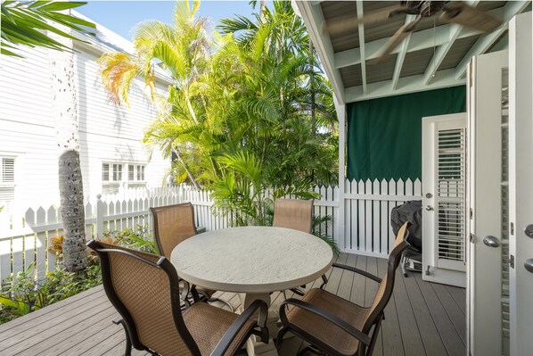 A round table with four chairs on a wooden deck, surrounded by a white picket fence and lush greenery. - High Tide at The Truman Annex in Key West (Key West)