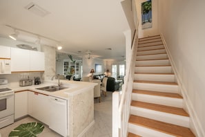 A modern kitchen with white cabinetry, a central island, and a dining area with a sofa and table.
