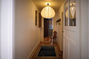 Un couloir doté d’un plancher en bois, d’un tapis, d’une chaise et d’un luminaire suspendu.