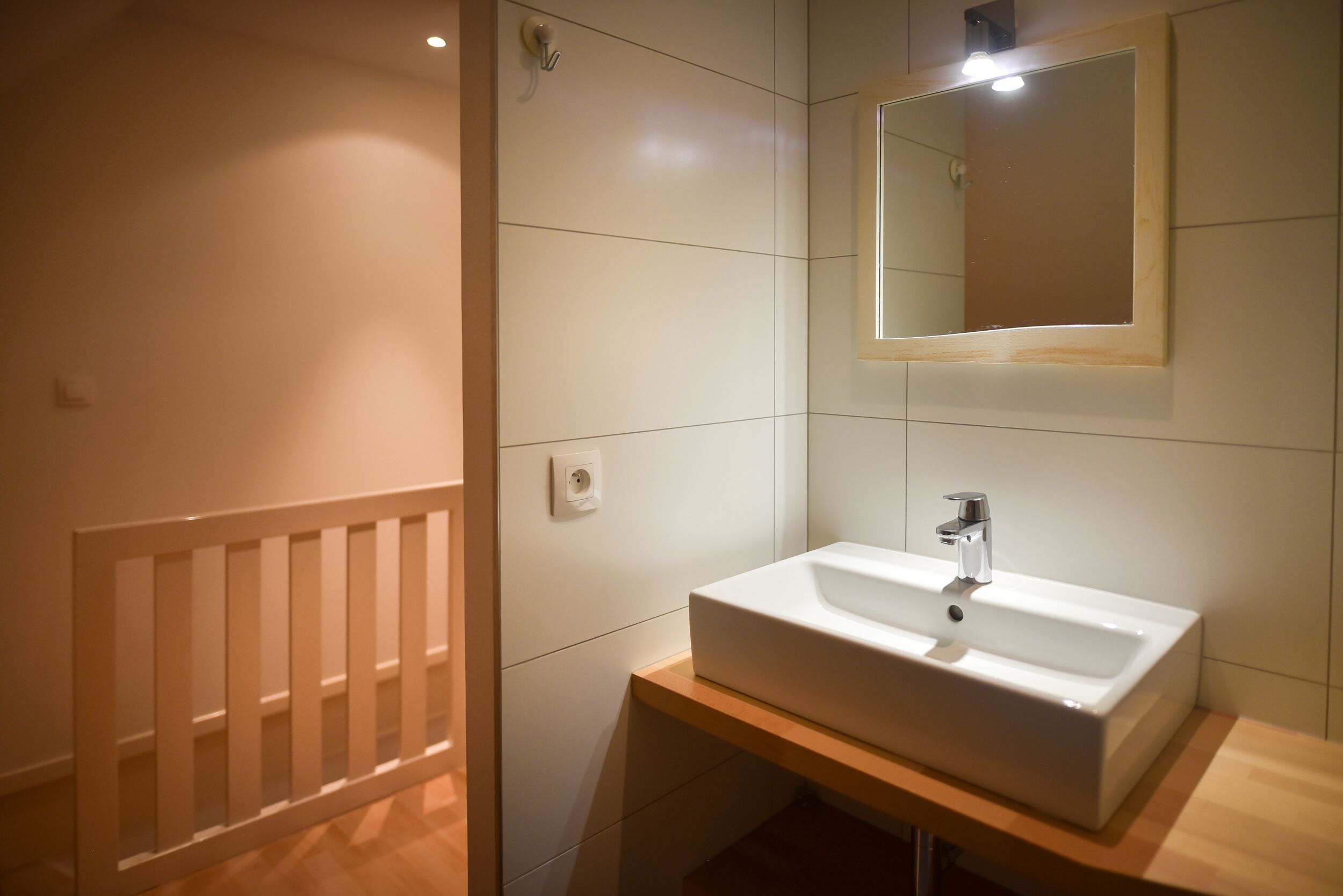 A modern bathroom with a white sink, mirror, and light fixture.