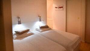 Een slaapkamer met twee eenpersoonsbedden, een nachtkastje, een wandlamp en een deur met een decoratieve versiering.
