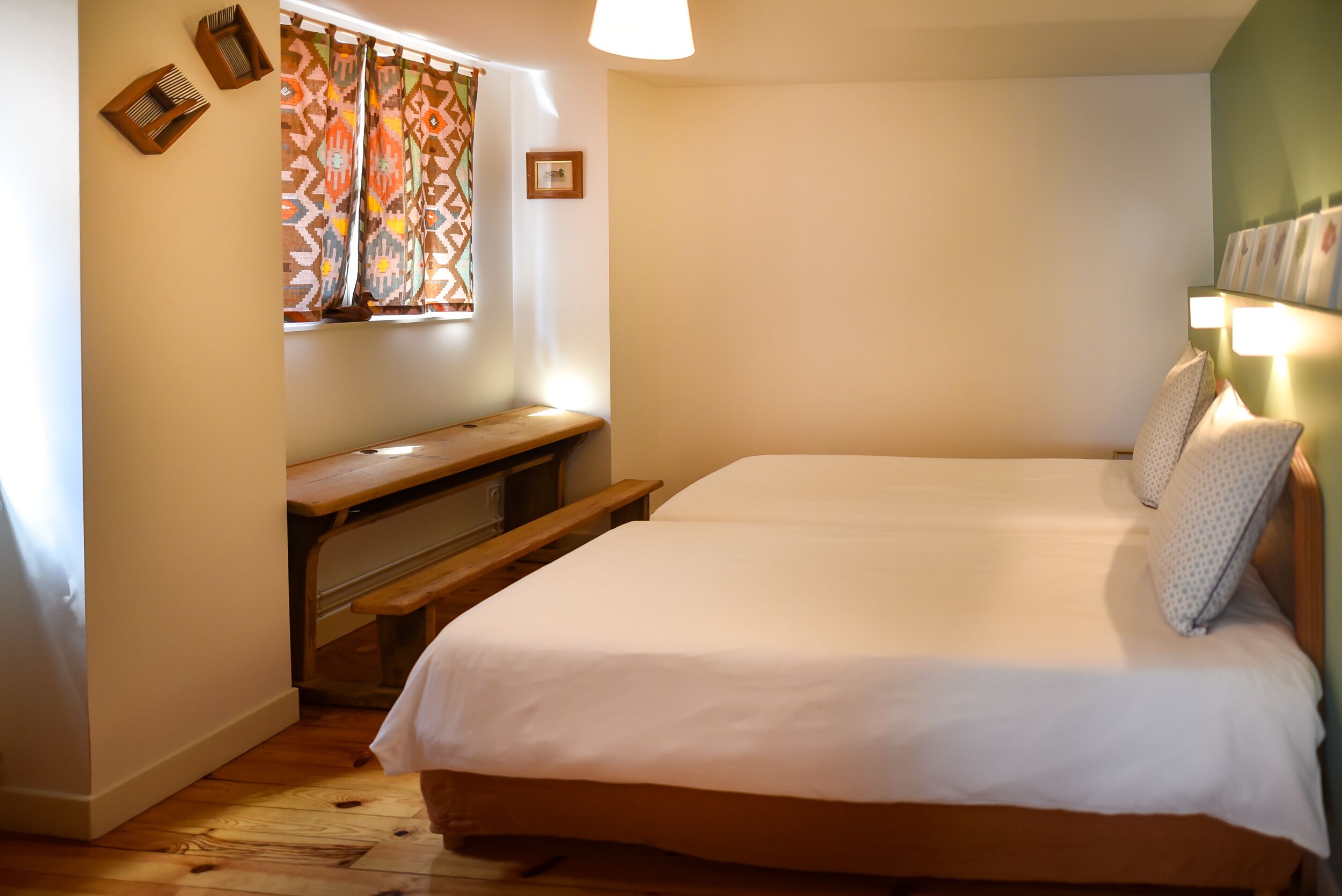 Ein Schlafzimmer mit einem großen Bett, einer hölzernen Bank, einem Fenster mit gemusterten Vorhängen und einer Wandleuchte.
