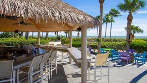 A beachside lounge with a thatched roof, outdoor seating, and a view of the ocean. - Sundial of Sanibel B307, Direct Beachview (Sanibel Island)