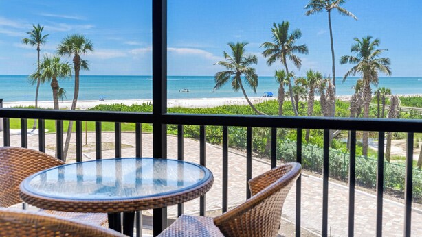 A balcony with wicker furniture overlooking a beach with palm trees and the ocean. - Sundial of Sanibel B307, Direct Beachview (Sanibel Island)