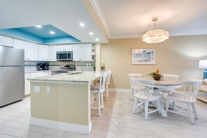 A modern kitchen with white cabinets, a central island, and a dining area with white chairs.