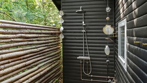 Una cabaña de madera con sistema de ducha integrado, que incluye un cabezal de ducha de mano y un cabezal de lluvia, montados sobre una pared de madera oscura.