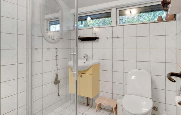 Um banheiro moderno com box de vidro, vaso sanitário branco, pia pequena bege e janela com vista para árvores.