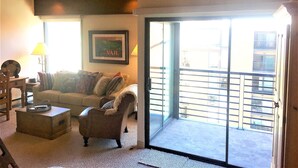 A living room with a wooden ceiling, a sofa, a chair, a table, and a balcony with a railing. - Pristine Condo, Walk To Lifts, 2 Fireplaces, 3 Balconies,  Mountain Views! (Vail)