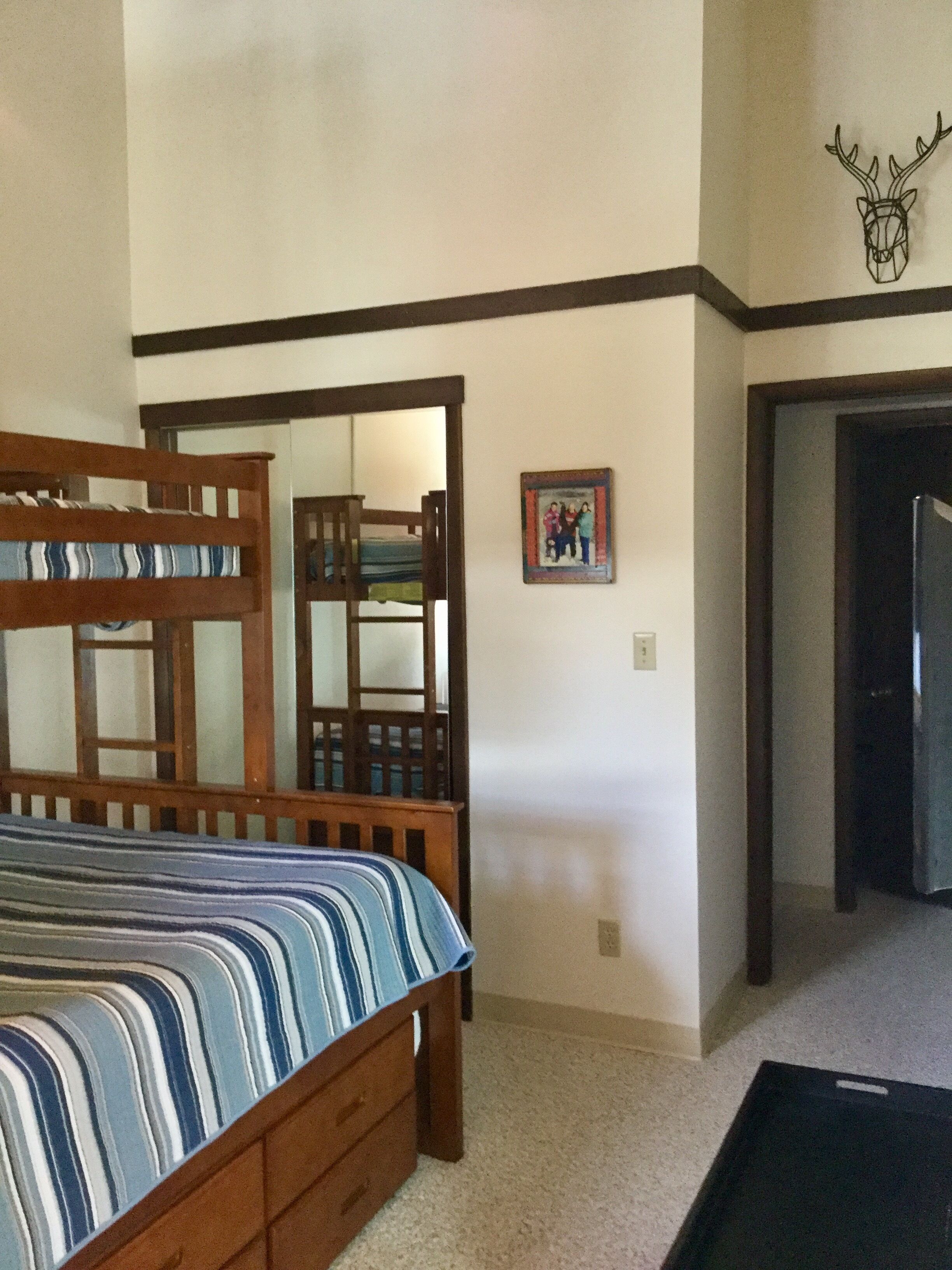 Un dormitorio con una cama litera, una pequeña foto enmarcada en la pared y una puerta que da a otra habitación.