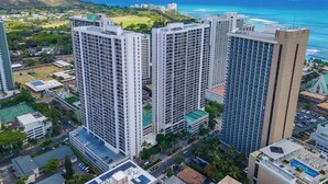 A high-rise building complex with multiple floors, surrounded by greenery and a view of the ocean. - Waikiki Banyan condo - ocean views & beach access (Honolulu)