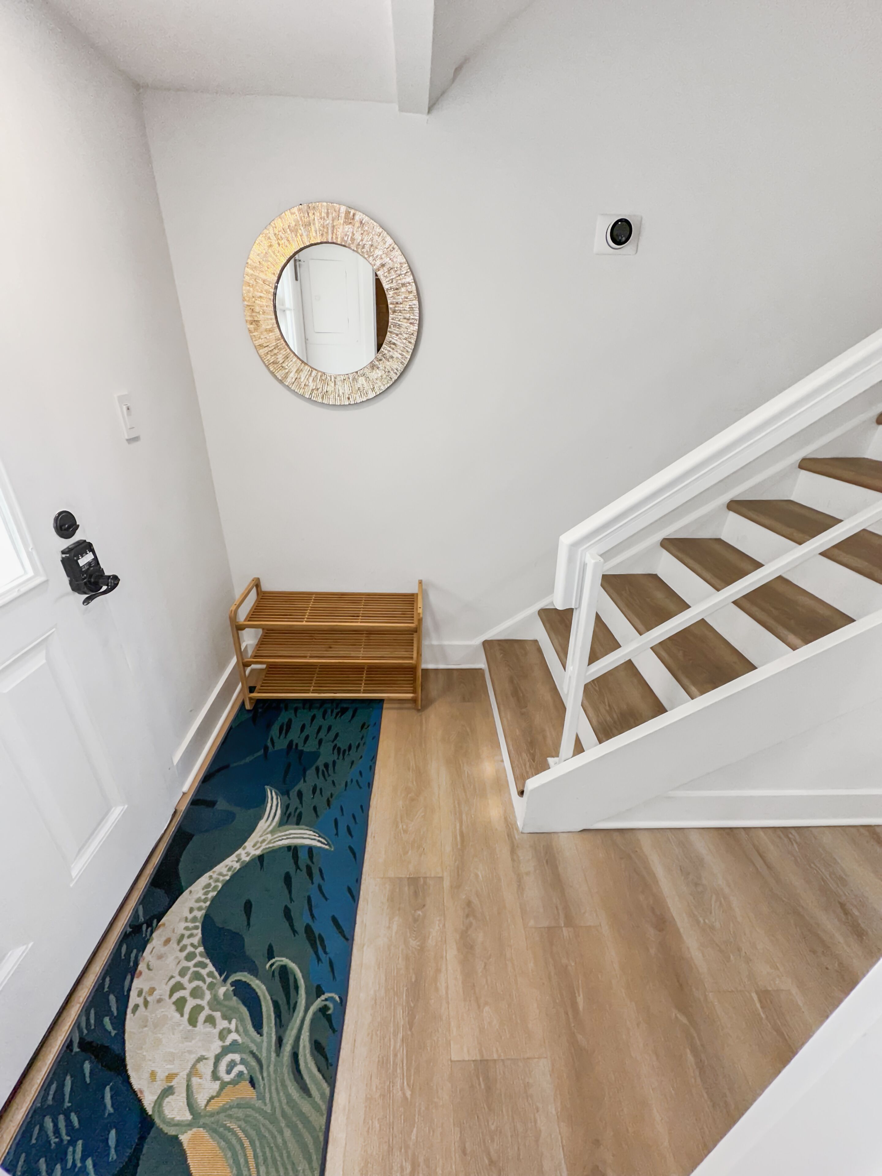 Una escalera con escalones de madera y barandillas blancas, que conduce a un rellano con un banco de madera y un espejo redondo en la pared.