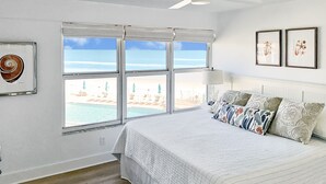 Un dormitorio con una cama grande, vista a la playa y un ventilador de techo.
