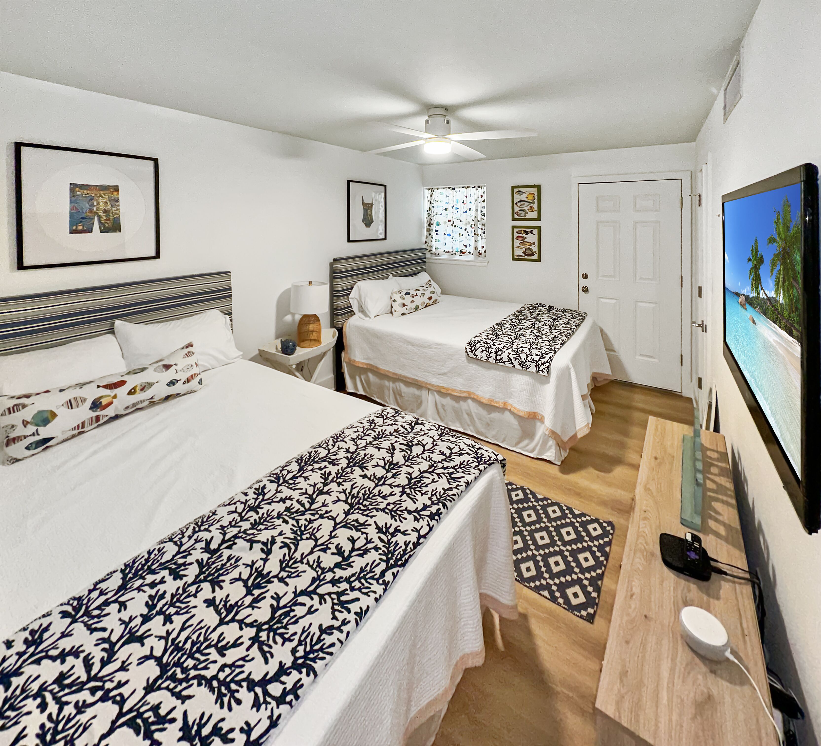 A hotel room with two beds, a ceiling fan, a TV, and a wooden side table.