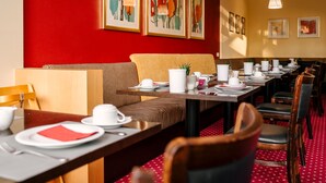 Restaurante com parede vermelha, obras de arte emolduradas e uma longa mesa de jantar posta com louça branca.