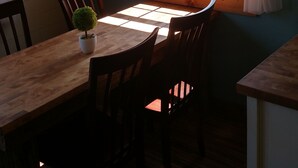 A dining area with a wooden table and chairs, a potted plant, and a window with a view of a grassy landscape.