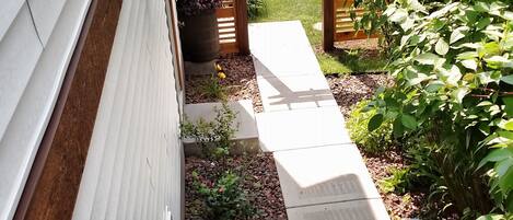 Un escalier mène à un patio couvert agrémenté d’une pergola, le tout entouré de verdure et d’un petit jardin.