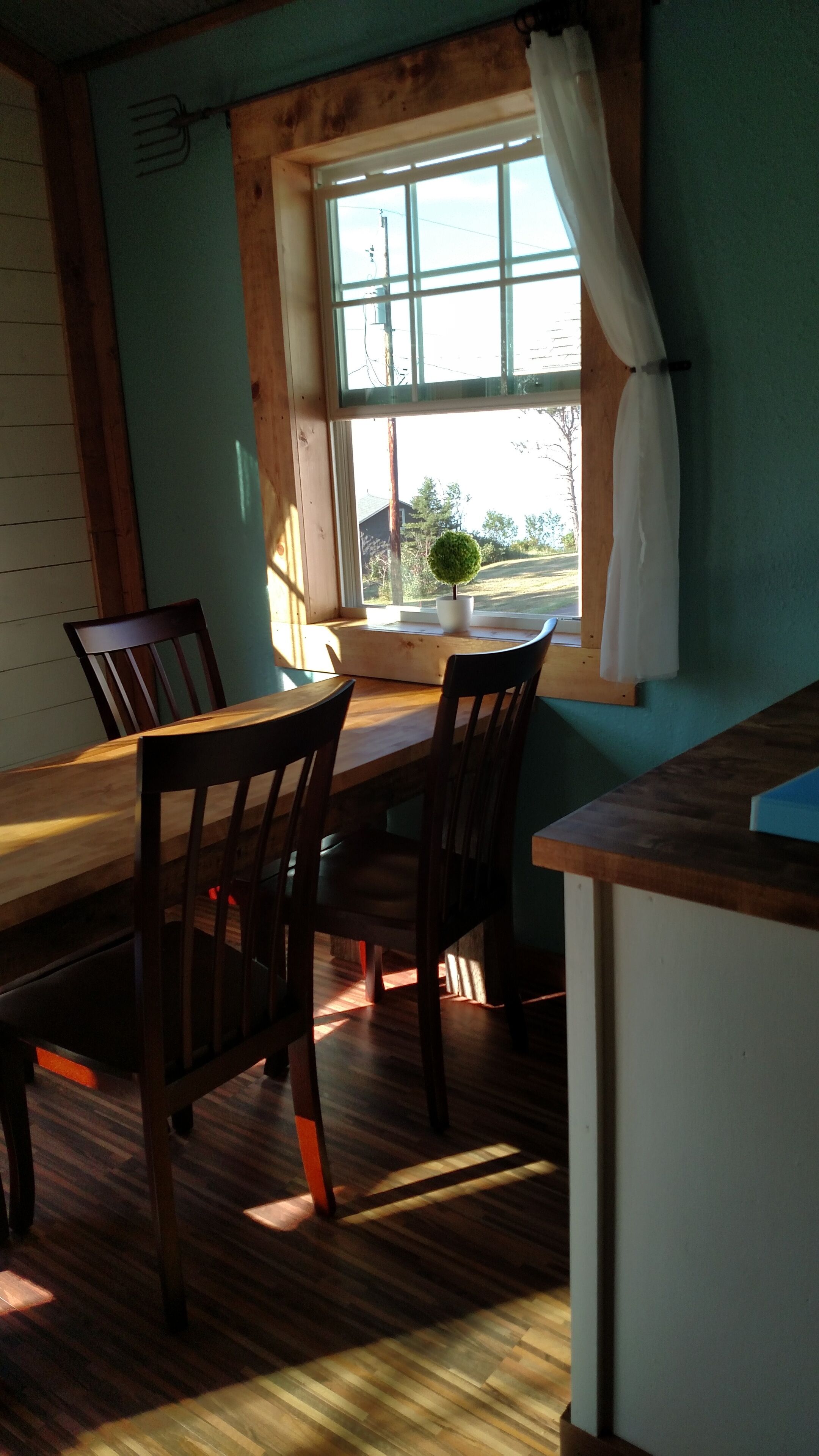 A dining area with a wooden table and chairs, a window with curtains, and a view of the outside.