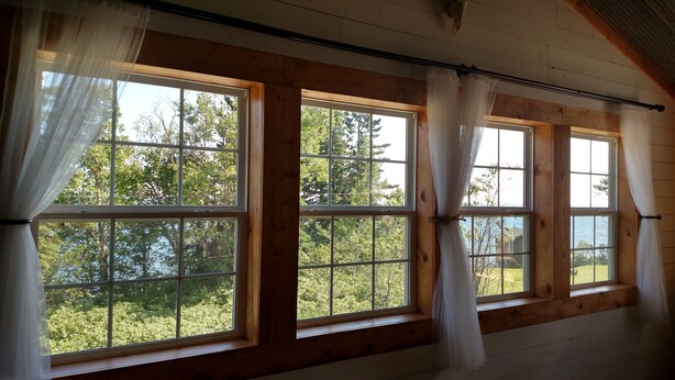 A room with large windows, wooden walls, and a view of trees and a body of water.
