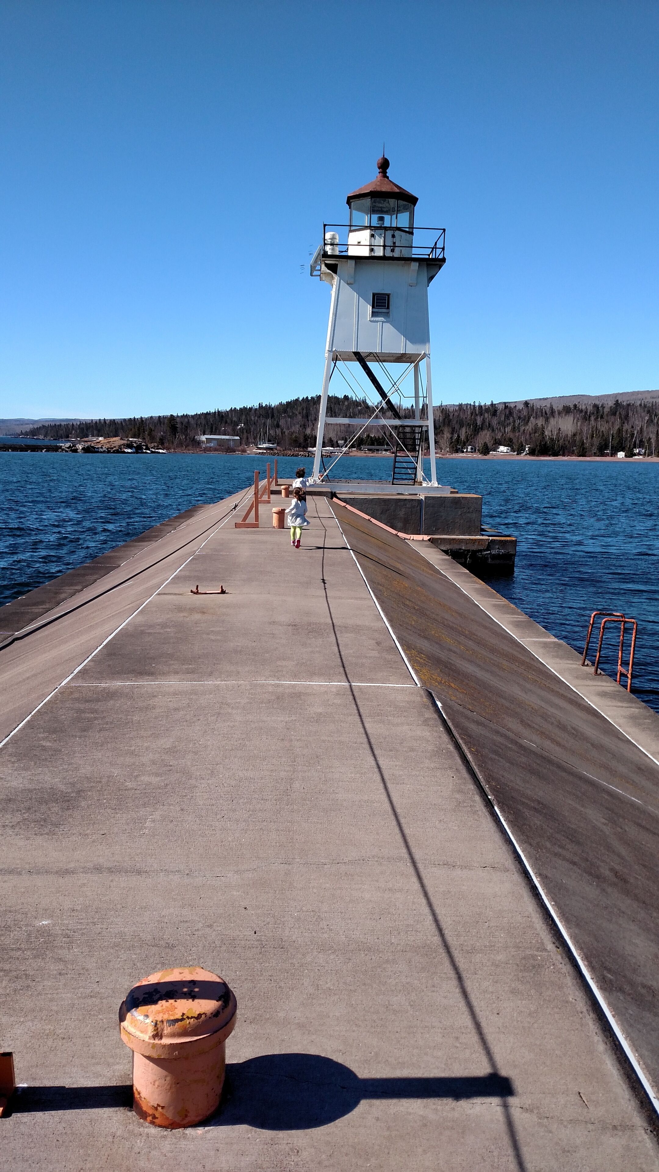 Un muelle que lleva a un faro, con vistas despejadas del agua y colinas boscosas al fondo.