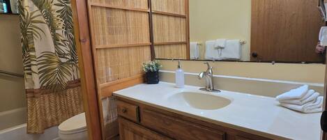 Un baño con tocador de madera, lavamanos, espejo con luces, inodoro y cortina de ducha.