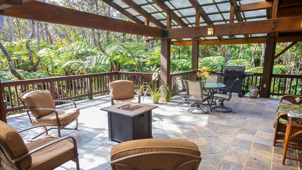 An outdoor patio with wicker furniture, a fire pit, and a grill area, surrounded by lush greenery. - Hale Mauna Loa Volcano Vacation Getaway-Upper Level Volcanoes National Park  (Volcano)