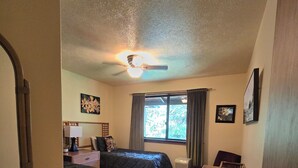 A bedroom with two beds, a ceiling fan, a window with curtains, a bedside table, and a small desk. - Hale Mauna Loa Volcano Vacation Getaway-Upper Level Volcanoes National Park  (Volcano)