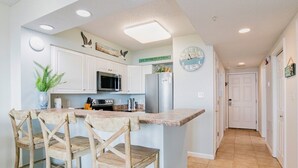A kitchen with white cabinets, a microwave, a refrigerator, and a clock on the wall. - Silver Beach 103 | Updated, Direct Beach Front, Pet Friendly! (Orange Beach)