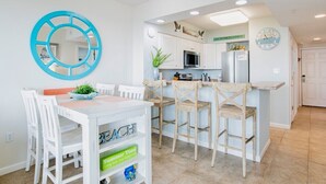 A kitchen with white cabinets, a microwave, and a refrigerator. There is a wooden island with bar stools and a clock on the wall. - Silver Beach 103 | Updated, Direct Beach Front, Pet Friendly! (Orange Beach)
