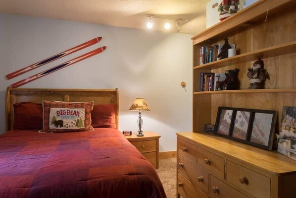 Une chambre à coucher avec un grand lit, une table de chevet, une commode en bois et une étagère avec des livres et des objets de décoration.