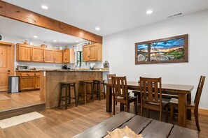 Une cuisine avec des meubles en bois, un coin repas avec une table et des chaises, et un tableau accroché au mur.