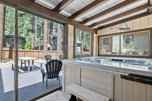 Un espace extérieur abrité comprenant un jacuzzi, une terrasse en bois et une vue sur la forêt environnante.