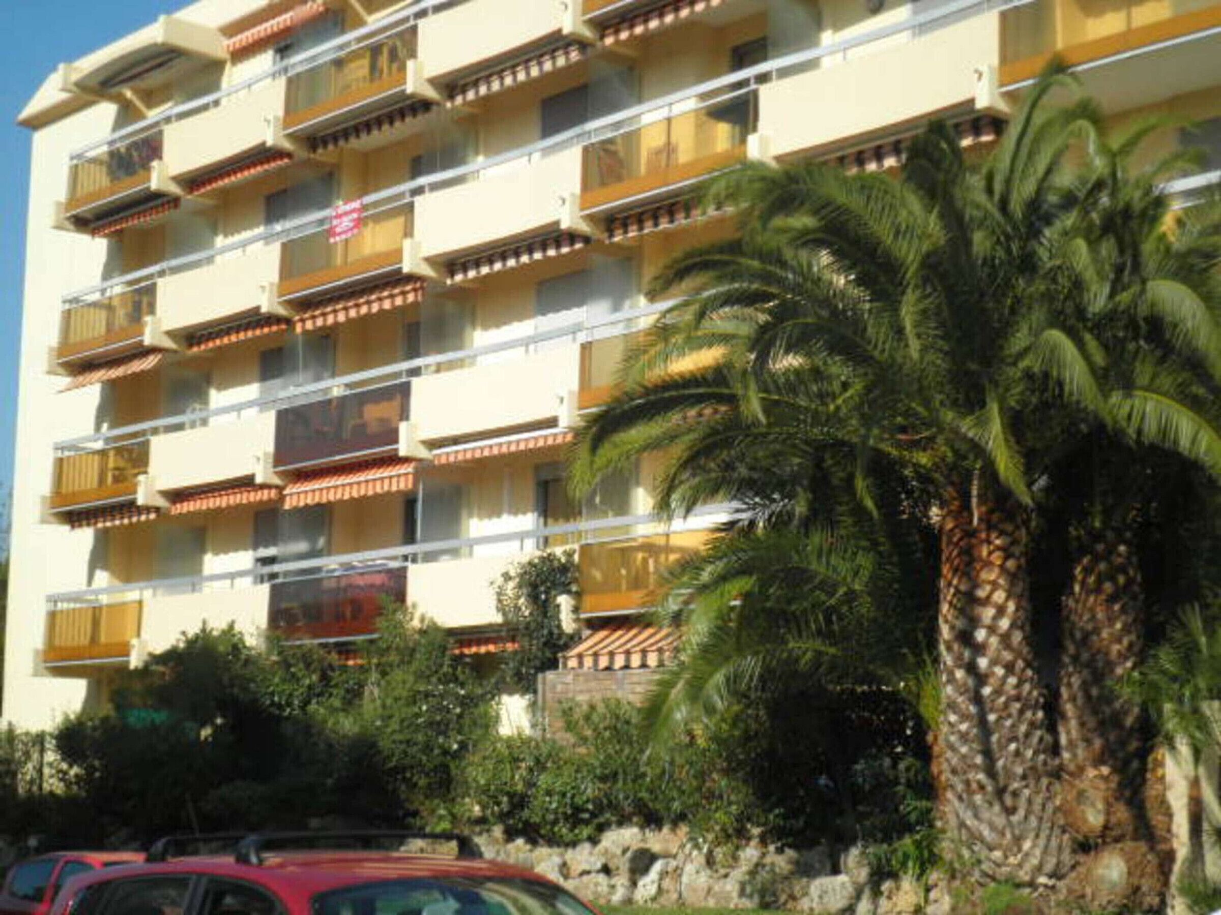 Un hôtel à plusieurs étages doté de balcons, de palmiers et d’un mur en pierre.