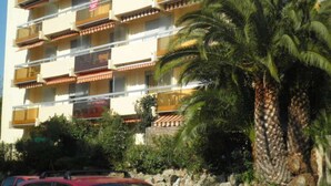 A multi-story hotel with balconies, palm trees, and a stone wall. - Cozy Studio Near Beach & Shops - Sleeps 2 (Fréjus)