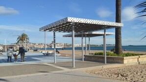 A beachside pavilion with a metal frame and a white roof, surrounded by sand and palm trees. - Cozy Studio Near Beach & Shops - Sleeps 2 (Fréjus)