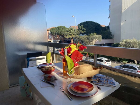 A balcony table set with plates, a wine bottle, a bowl, a knife, a fork, and a magazine.
