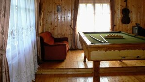 Une pièce en bois avec une table de billard, un fauteuil rouge et une fenêtre avec des rideaux.