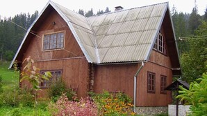 Une maison en bois avec un toit en pente, entourée de verdure et d’un petit jardin.