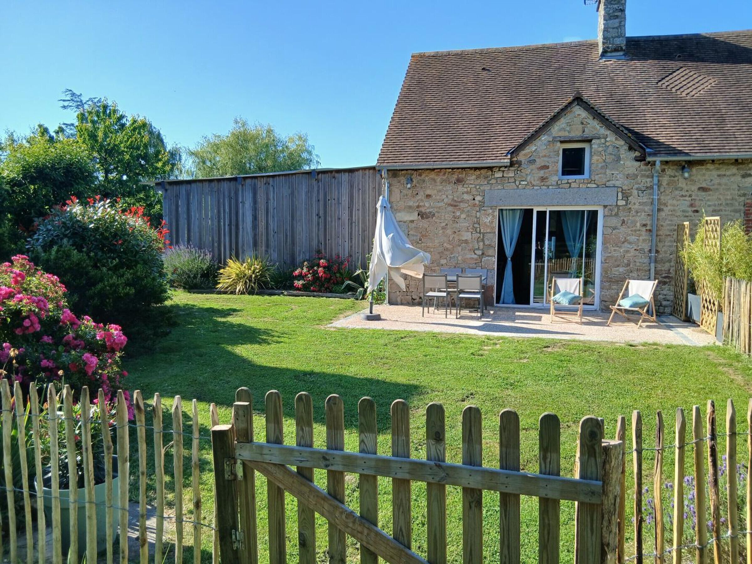 Une maison en pierre avec un jardin, une clôture en bois et du mobilier d’extérieur.