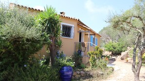 A house with a tiled roof, a window with a metal grill, and a door. There is a large blue barrel and a tree in front of the house. - PORTO-VECCHIO - 5 MIN FROM PALOMBAGGIA BEACHES<br> (Porto-Vecchio)