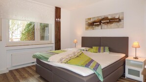 Een slaapkamer met een groot bed, twee nachtkastjes met lampen, een raam met uitzicht op groen, en een schilderij aan de muur.