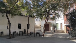 A quiet street with benches and trees lining the sidewalk, a white building with a red door, and a balcony with red flowers. - Blau Masnou (El Masnou)