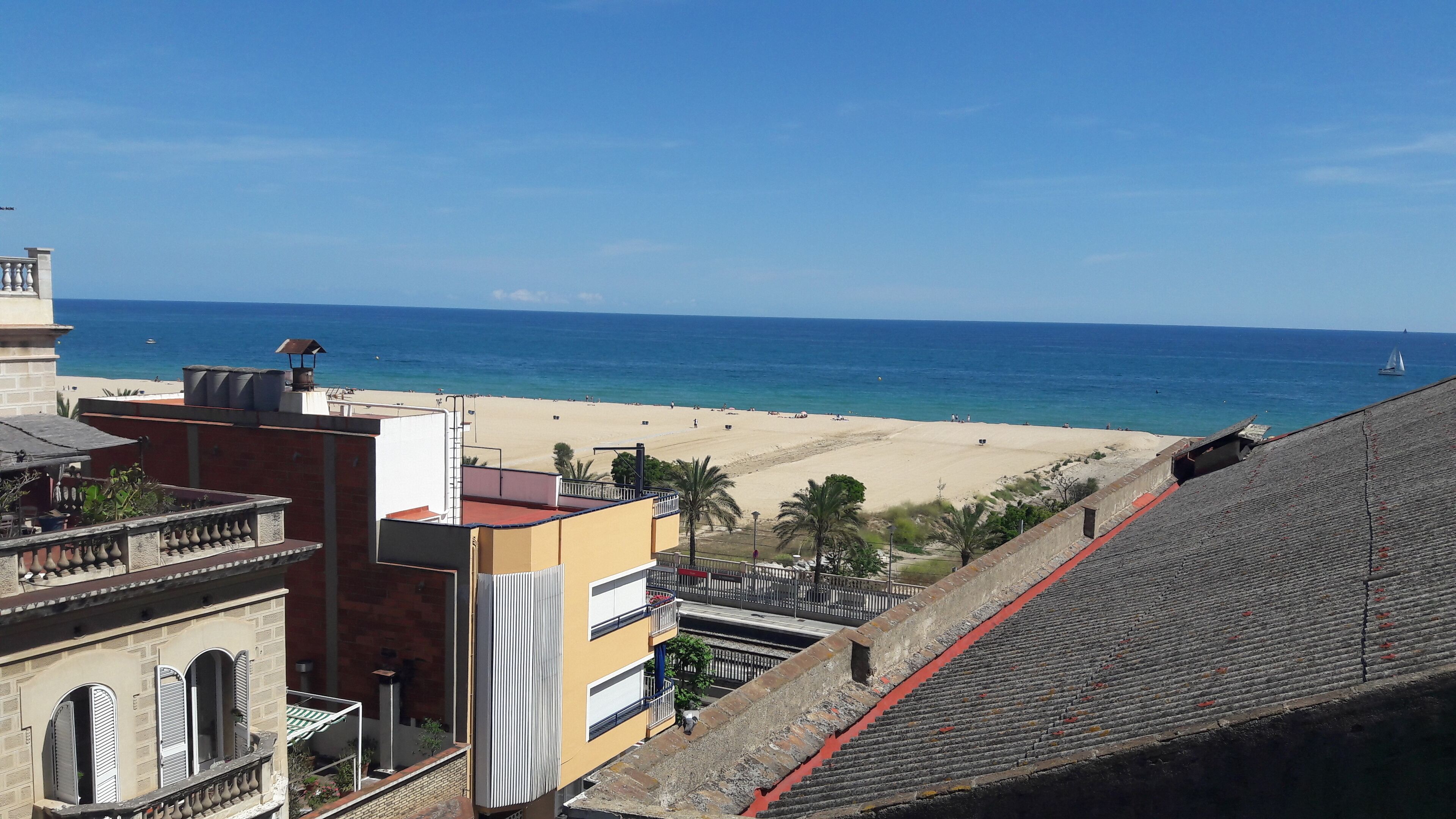 Une vue côtière avec une plage, des bâtiments et un voilier.