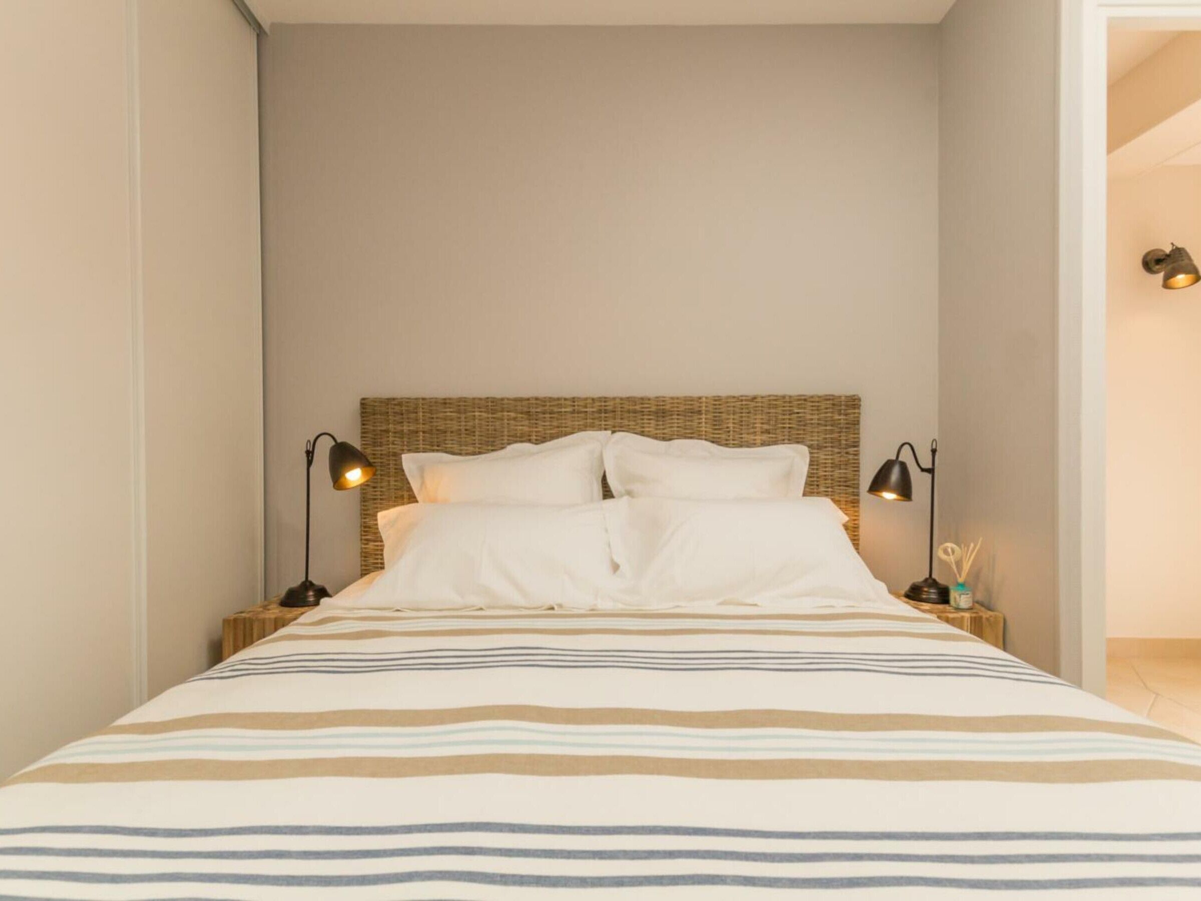 A neatly made bed with striped bedding, two bedside lamps, and a wicker headboard.